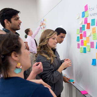 Students at a whiteboard arranging brightly colored sticky notes as part of a design thinking project