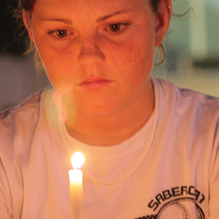 Close up of female TCU student looking thoughtful as she holds a candle before her face.